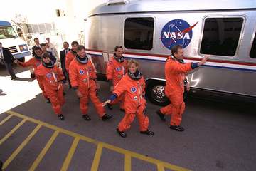 The STS-94 crew walks out of the Operations and Checkout Building and heads for the Astrovan that will transport them to
