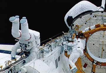 Astronauts Gregory J. Harbaugh, wearing extravehicular mobility unit (EMU) (red stripes), and Mario Runco, Jr. during th