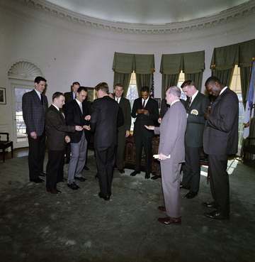 President John F. Kennedy (center left, back to camera) hands items to members of the National Basketball Association (N