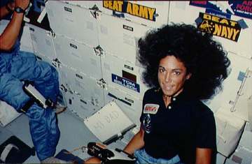 View of Mission Specialist Judith Resnik sitting on the floor of the middeck. Beside her on a notebook is a note which s