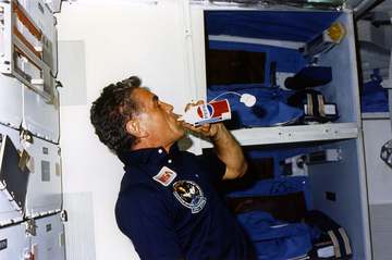 Karl Henize, STS-51F mission specialist, drinks from a Pepsi can on the mid-deck of space shuttle Challenger