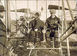 Wilbur and Katharine Wright seated in the Wright Model A Flyer with Orville Wright standing nearby. This was Katharine's