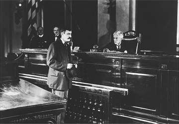 Warren Cook, an actor, stands in front of Judge Mountain Landis's bench in the 1917 government film, The Immigrant.
