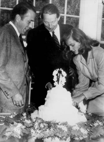Photo of the wedding of Humphrey Bogart and Lauren Bacall in 1945. Caption reads as follows:Bogart–Bacall Wedding CakeGr