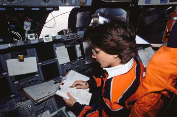 Astronaut Nancy J. Currie, STS-109 mission specialist, looks over a procedures check list while occupying the pilot’s st