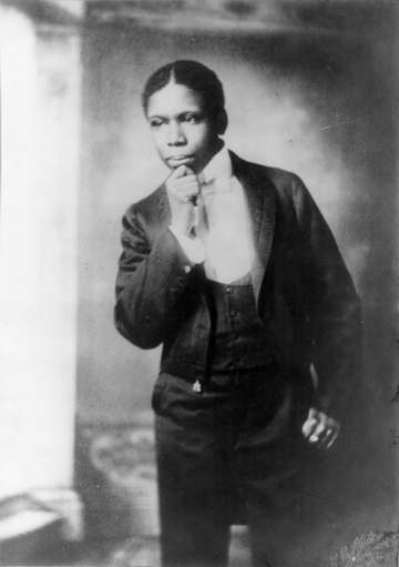 Paul Laurence Dunbar, three-quarter length portrait, standing, facing left, hand on chin