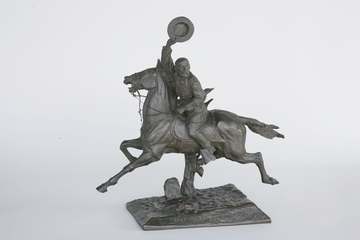 A bronze sculpture of a man in Civil War-era uniform on horseback. He holds the reins with his left hand and holds his h